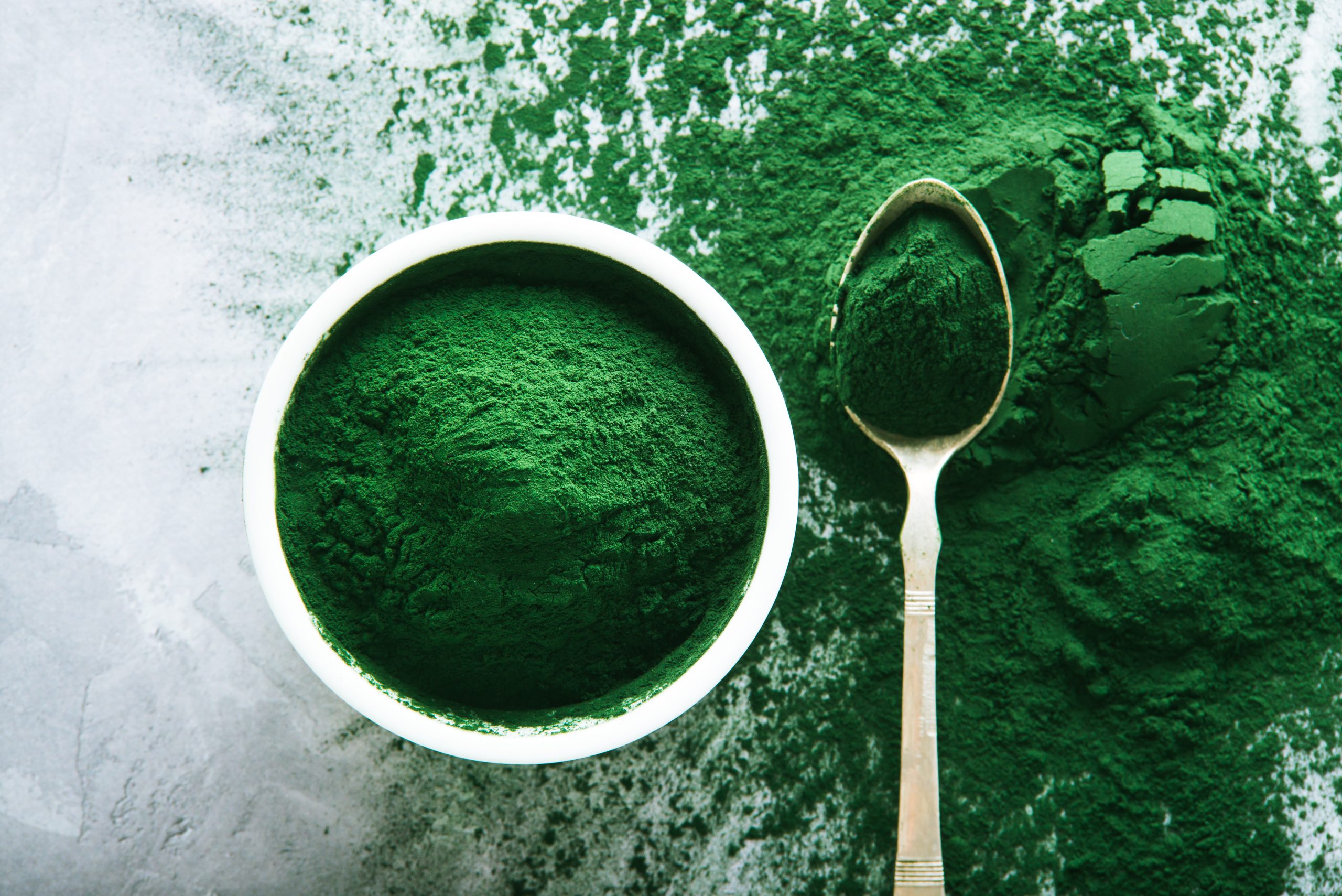 spirulina-powder-white-plates-scattered-green-background alga spirulina
